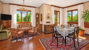 A dining room with a table set for four, surrounded by floral-patterned chairs, a chandelier, and a view of greenery outside. - Villa La Verbanina Private Garden, Ghiffa, Italy (Ghiffa)