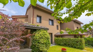A two-story building with a flat roof, a covered patio area, and a well-maintained garden with a lawn and flower beds.