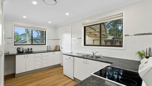 Una cocina moderna con armarios blancos, encimera negra, lavavajillas integrado y un amplio ventanal con vistas al exterior.