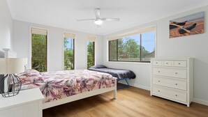 Un dormitorio con cama, cómoda, ventilador de techo y ventanas amplias.