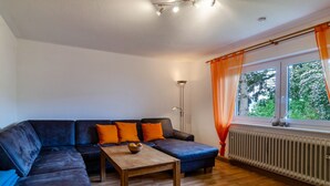 A living room with a sectional sofa, a wooden coffee table, a floor lamp, and a window with curtains.