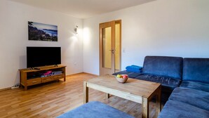 A living room with a television, sofa, and a small table with a bowl of fruit.