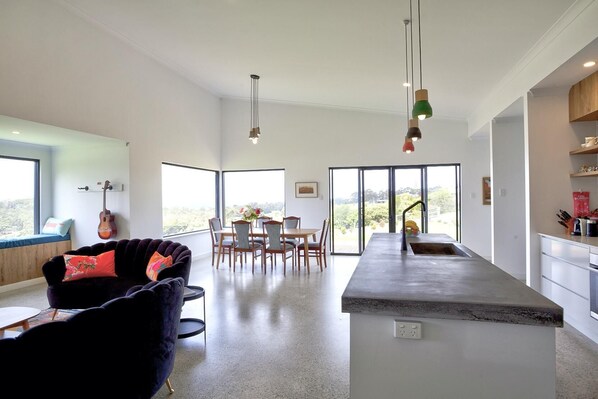 A modern kitchen with a central island, dining area with chairs, and a sofa with cushions.