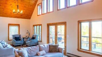 A spacious living room with a high ceiling, large windows, a wooden coffee table, and a sofa set.