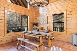 L’intérieur d’une cabane en bois, avec une table à manger, des bancs et un ventilateur de plafond.