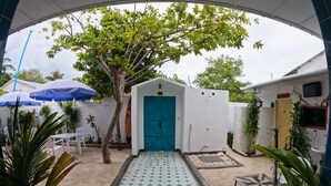 A courtyard with a blue door, white walls, and a tiled floor. There are umbrellas, chairs, and plants around. - Adroit Beach Inn (Guraidhoo)