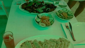 A dining table with various dishes, including flatbreads, salads, and a beverage. - Adroit Beach Inn (Guraidhoo)