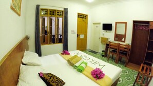 A hotel room with a bed, a desk, a chair, a wardrobe, and a television. - Adroit Beach Inn (Guraidhoo)