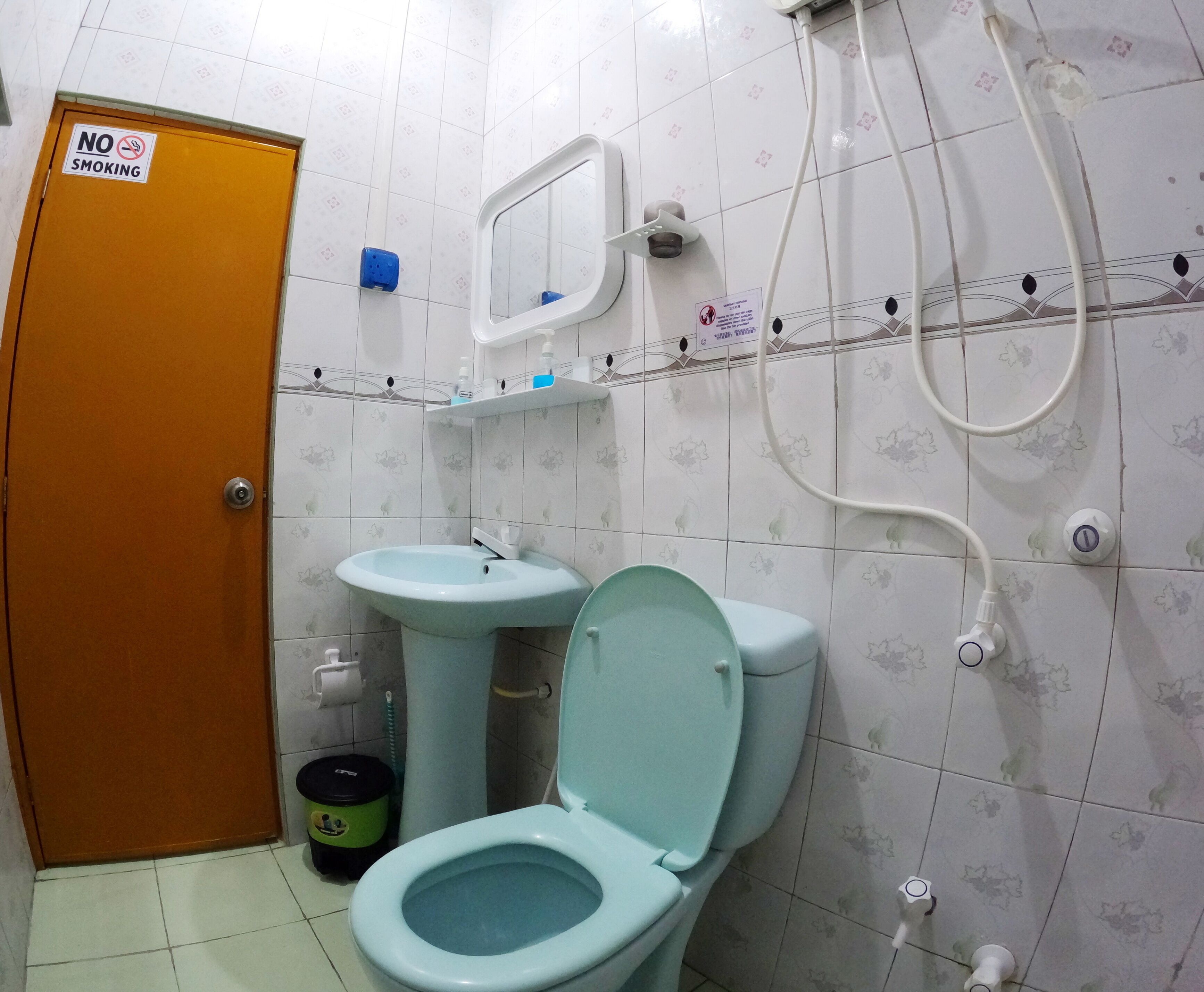 Une salle de bain équipée de toilettes, d’un lavabo et d’une douche. Un panneau « Il est interdit de fumer » est affiché sur la porte.