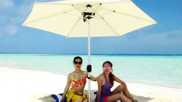 Guests can relax under a shaded umbrella on the sandy beach.