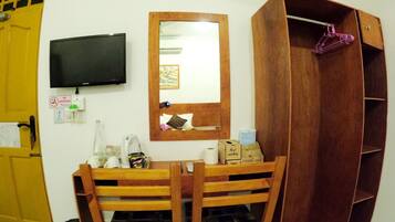 A room with a wooden desk, a mirror, a television, and a wardrobe.