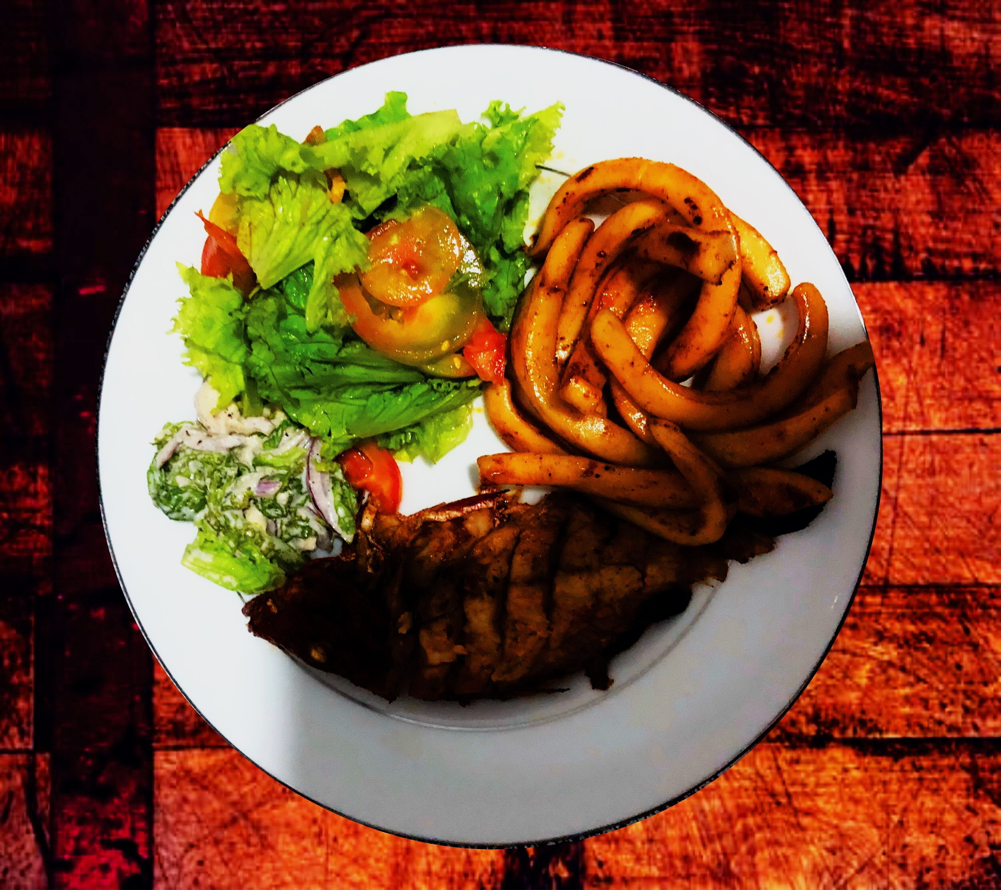 Un piatto con carne alla griglia, cipolle saltate, lattuga e pomodori.