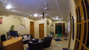 A reception area with a wooden reception desk, black and white patterned sofas, a potted plant, and a green exit door. - Adroit Beach Inn (Guraidhoo)