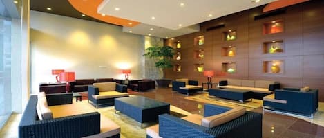 A modern lobby with seating areas, a large plant, and wall-mounted lighting.