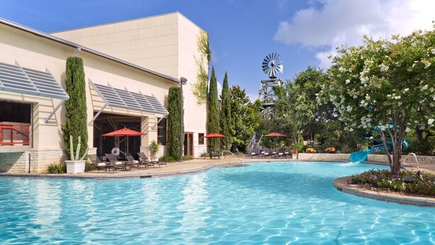 A swimming pool with lounge chairs and umbrellas, a windmill, and a building with a sloped roof.