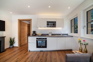 A modern kitchen with built-in appliances, a wooden floor, and a view through a window.