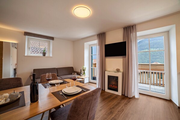A dining area with a table set for two, a sofa, a fireplace, and a TV mounted on the wall.