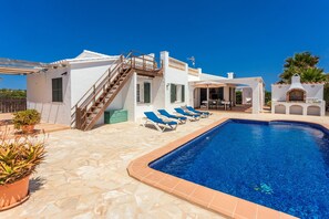 A poolside area with a clear blue pool, a white building with a staircase, and a small structure with a chimney.