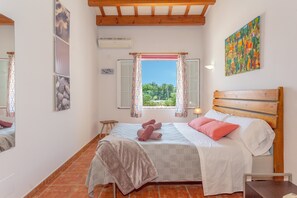 A bedroom with a bed, a window with curtains, a wooden headboard, and a painting on the wall.
