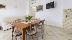 Un comedor con una mesa de madera, cuatro sillas, un control remoto y una planta en maceta.