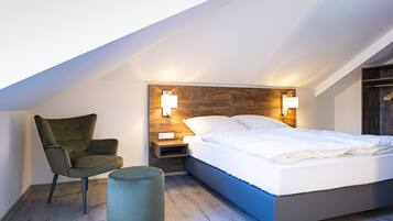 A modern bedroom with a sloped ceiling, a bed with white bedding, a green upholstered chair, and two bedside lamps.