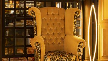 Ein vielfach verziertes Armchair mit einem gemusterten Kissen in einem wohlig beleuchteten Raum mit einem gemusterten Boden und einer Glasabtrennung.