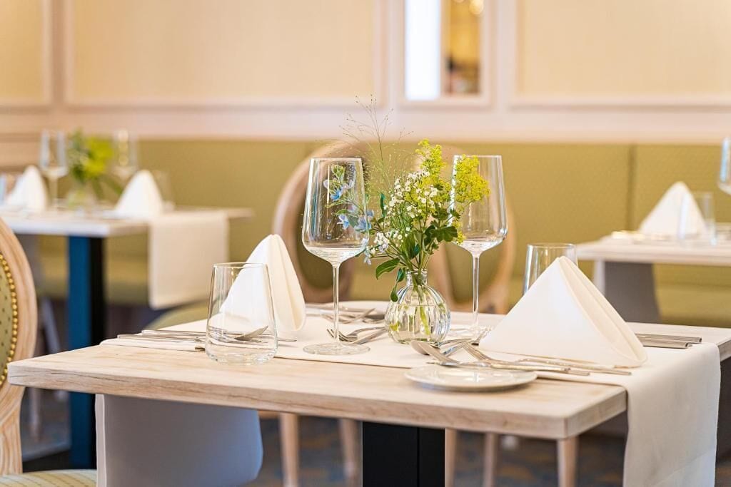 A dining table set with clear glassware, a vase with flowers, and white napkins.