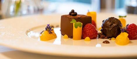 A dessert plate with a chocolate mousse, raspberries, and yellow fruit pieces.