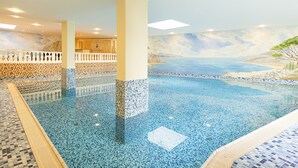 An indoor swimming pool with mosaic tiles, a tiled deck, and a mural of a beach scene.