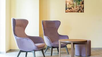 Two purple chairs and a small wooden table in a room with a light yellow wall and a painting of a forest.