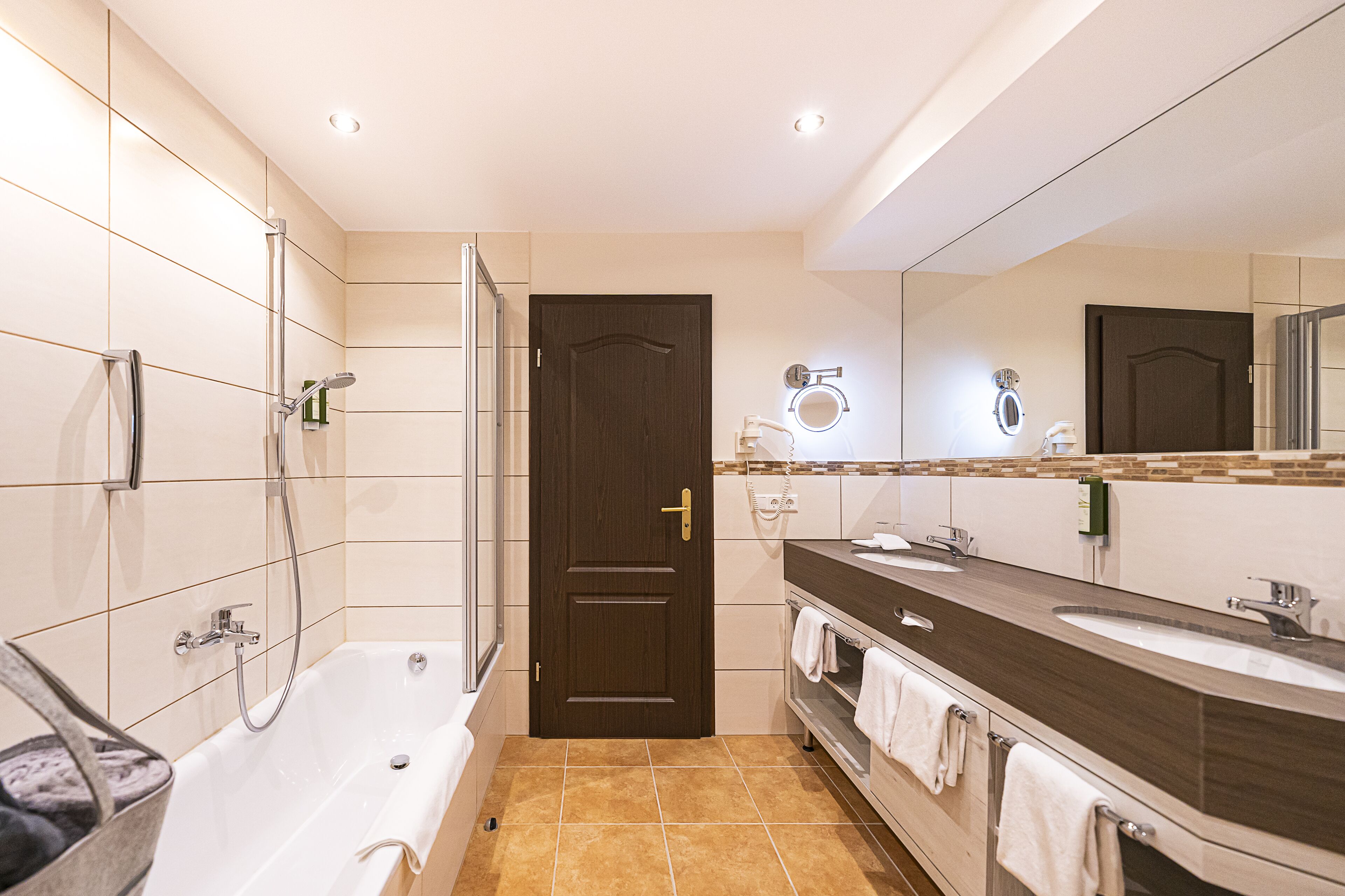 Une salle de bain moderne équipée d’une baignoire, d’une douche, d’un meuble-lavabo avec un miroir et d’une porte.