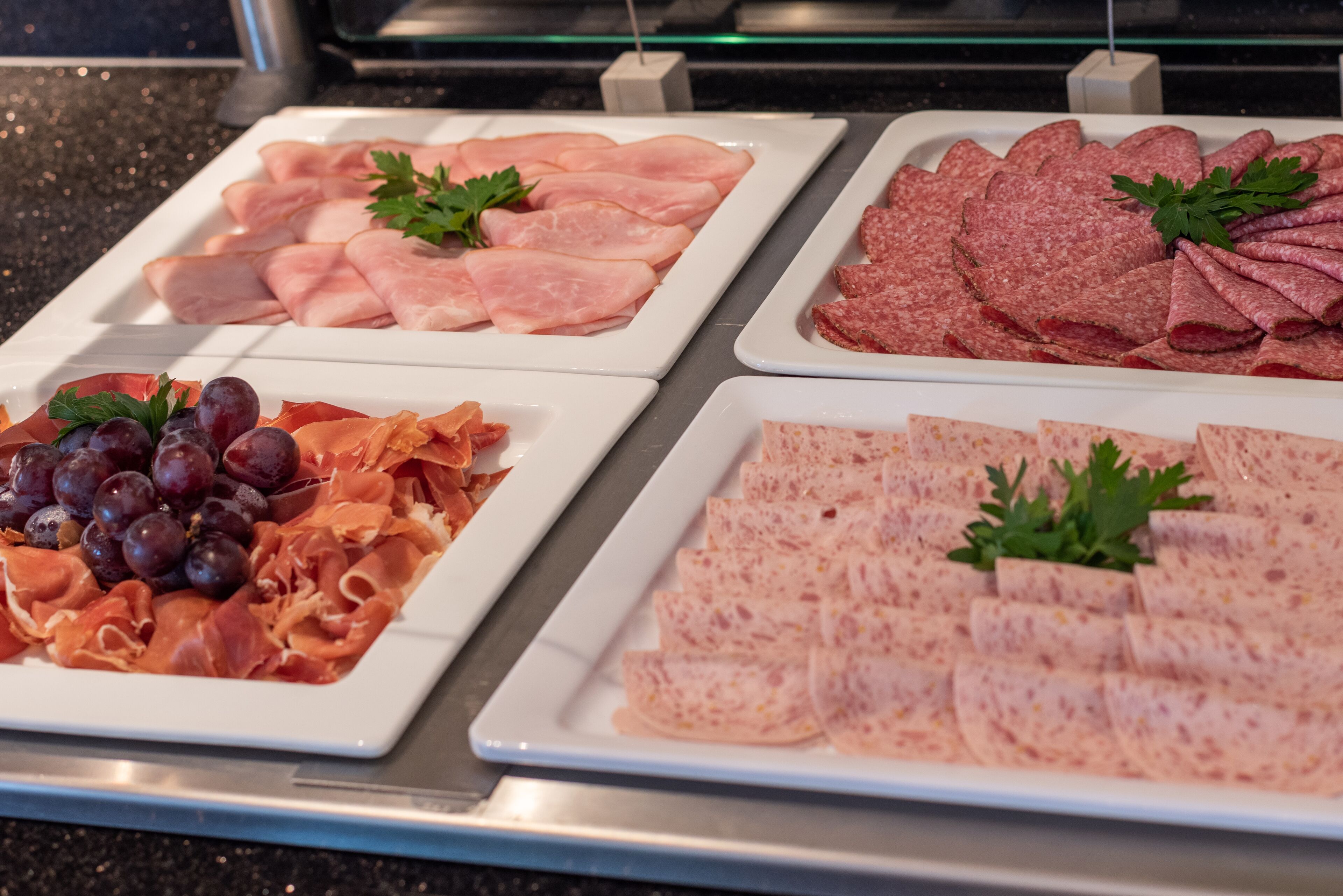 Un bufé con diversos tipos de embutidos y quesos, incluyendo jamón, salami y una preparación con uvas y prosciutto.