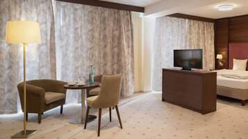 Une chambre d’hôtel avec un lit, un bureau avec une télévision, une lampe, deux chaises et une petite table sur laquelle se trouvent une bouteille et un verre.