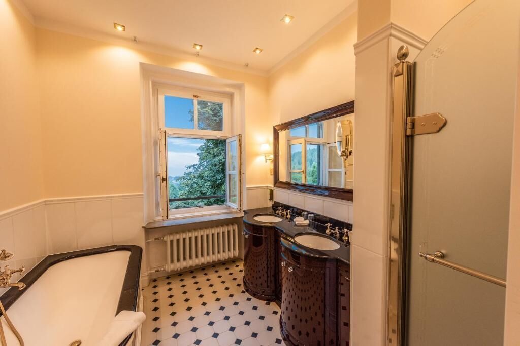 Un baño con bañera, dos lavamanos, una ventana y un radiador.
