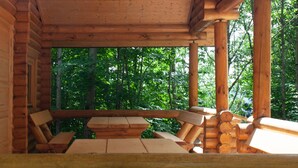 A wooden cabin with a covered porch, log benches, and a view of the forest.