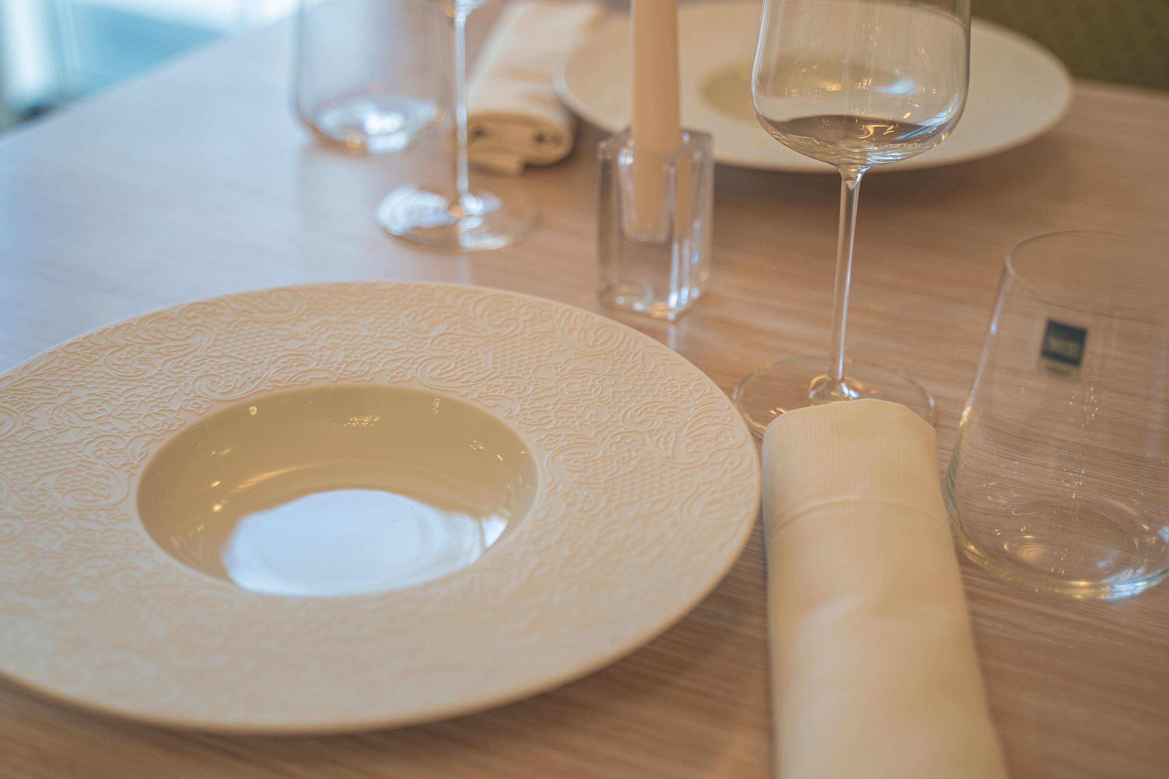 A table set with a white plate, a rolled napkin, and a glass of water.