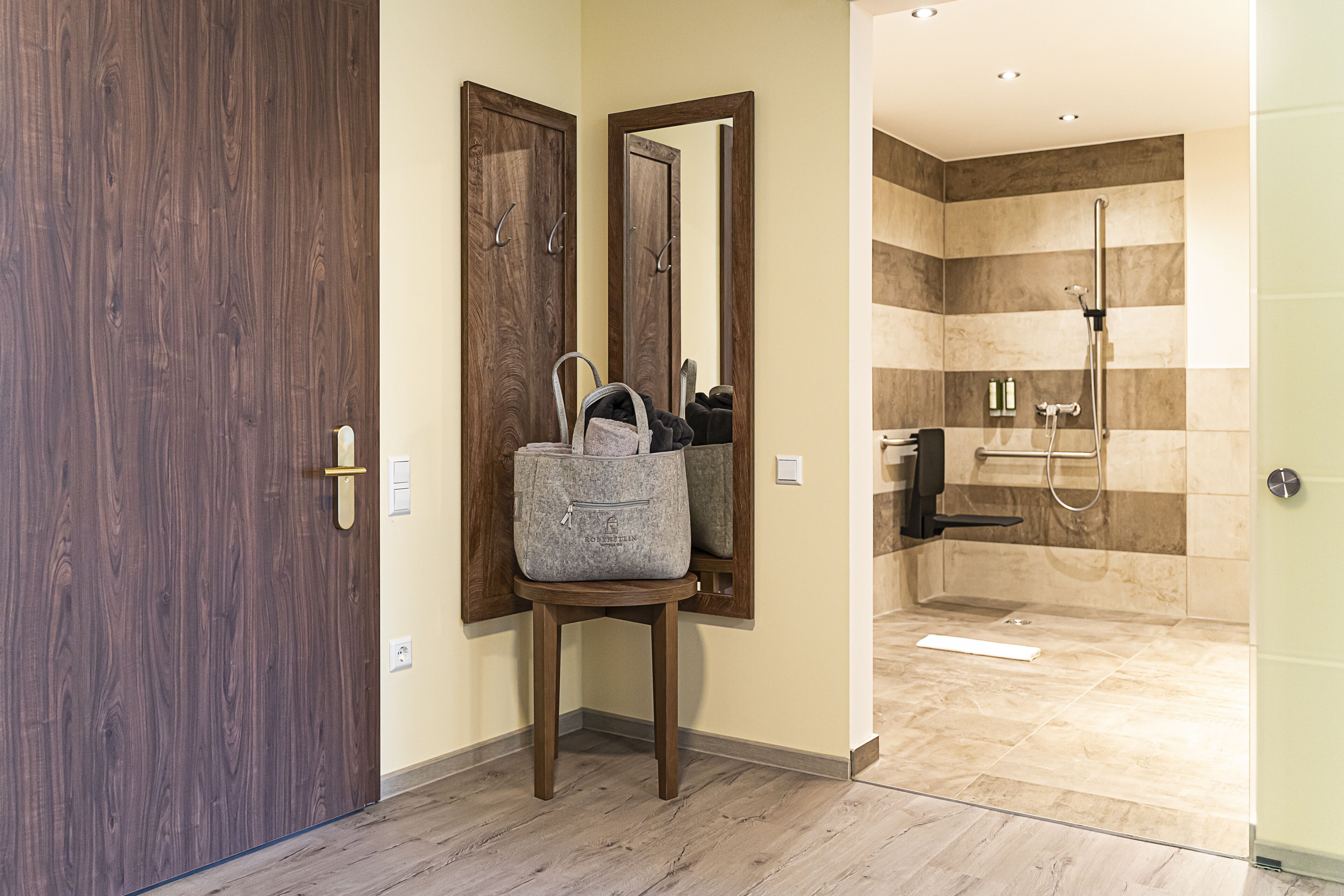 A hotel bathroom with a shower, a mirror, and a wooden door.