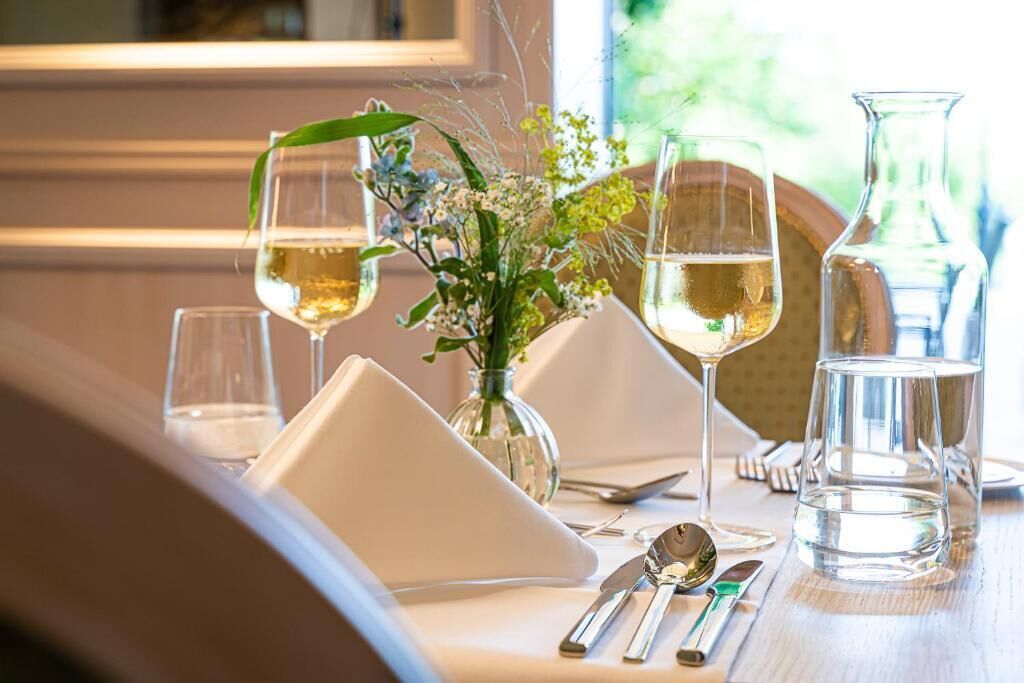 A table set for dining with wine glasses, a vase with flowers, and a pitcher of water.