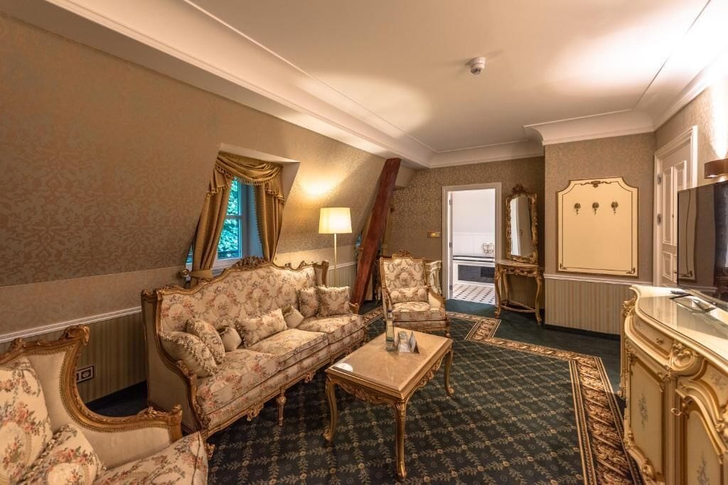 A room with a sofa, armchair, and a small table. There is a mirror and a door in the background.