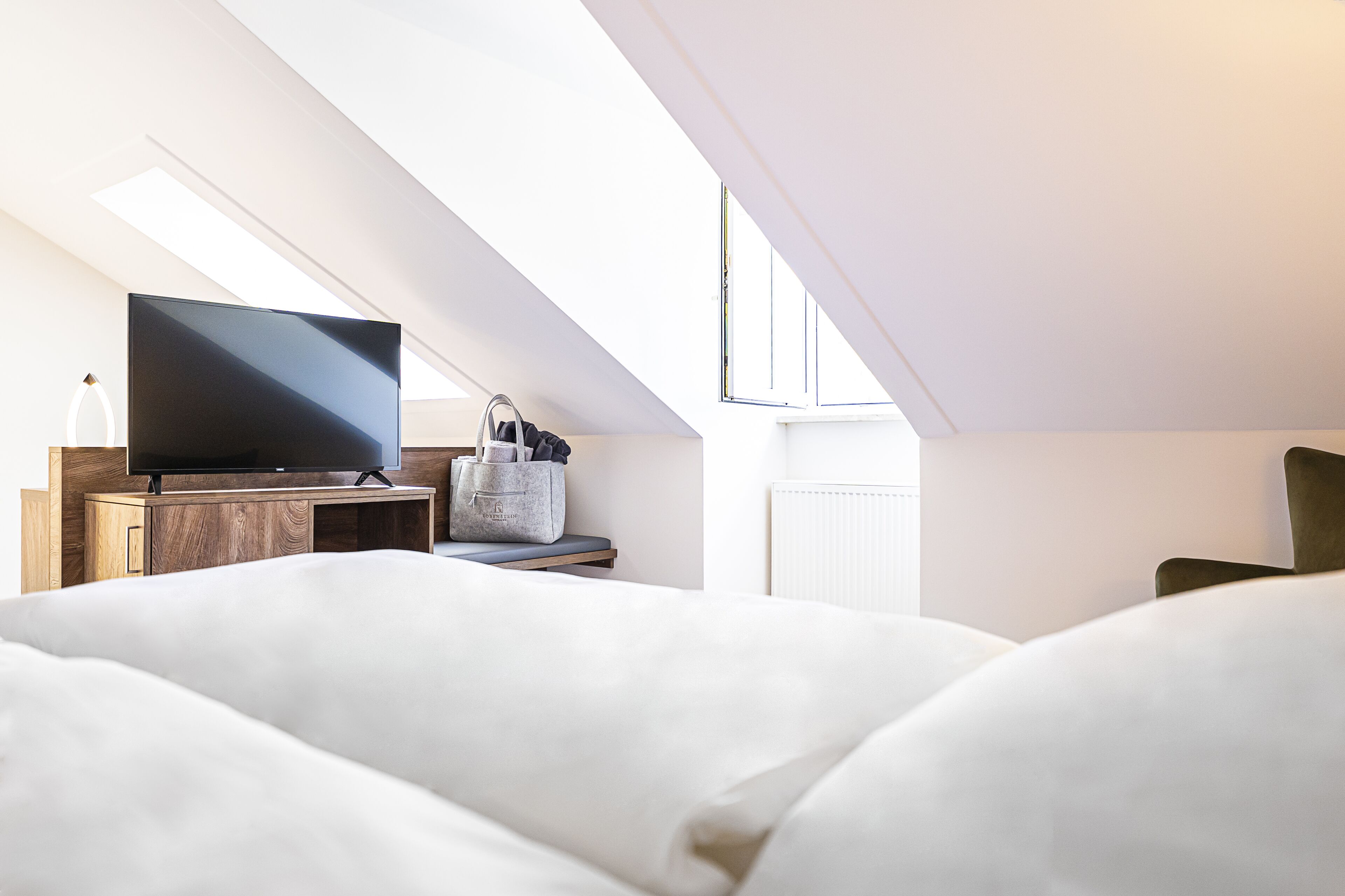 Un dormitorio moderno con una televisión de pantalla plana sobre un mueble de madera, una cesta gris de almacenamiento y un amplio ventanal que proporciona luz natural.