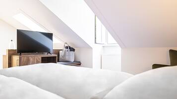 Un dormitorio moderno con una televisión de pantalla plana sobre un mueble de madera, una cesta gris de almacenamiento y un amplio ventanal que proporciona luz natural.