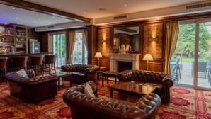 A spacious lounge area with leather sofas, a bar with shelves of bottles, and a fireplace.
