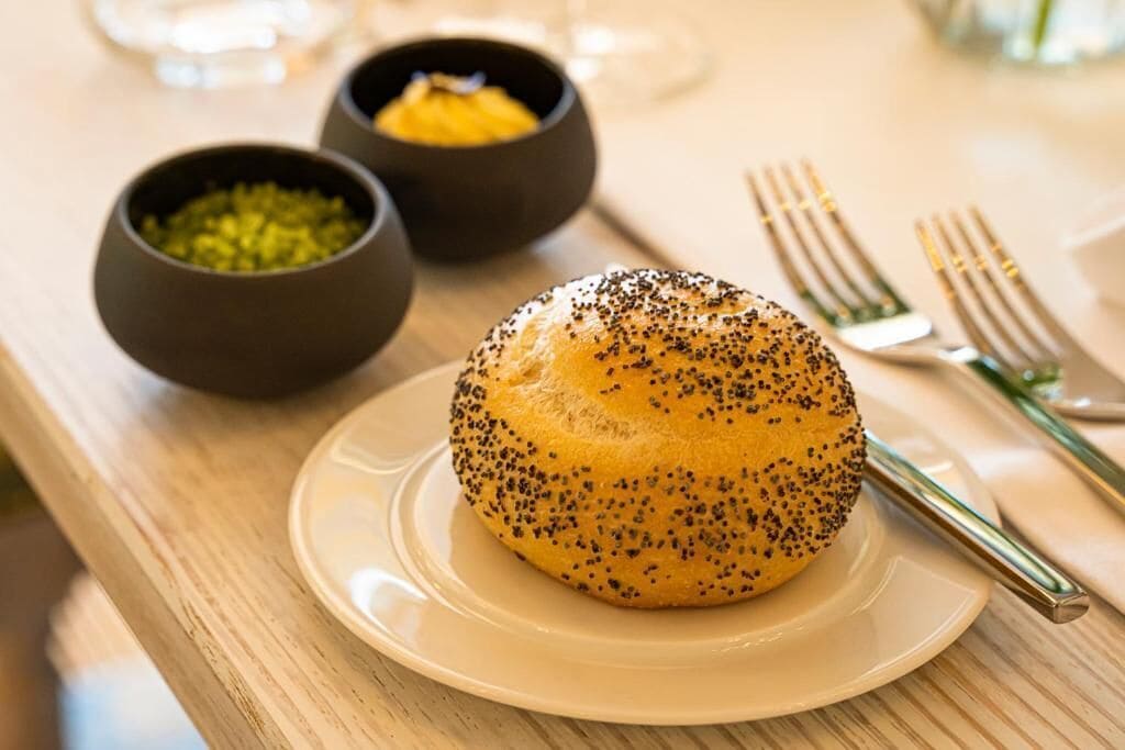 A table with a plate of poppy seed rolls, two small bowls with condiments, and a fork.
