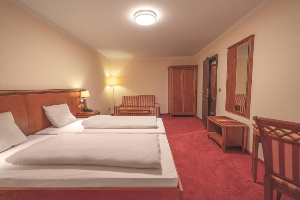 A hotel room with two beds, a nightstand with a lamp, a chair, a wardrobe, and a mirror.