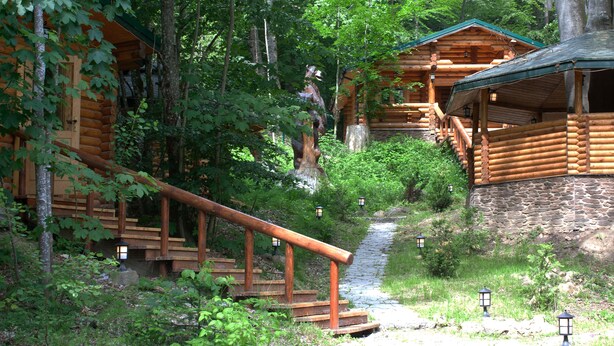 A log cabin with a stone foundation, wooden stairs, and a small stream.