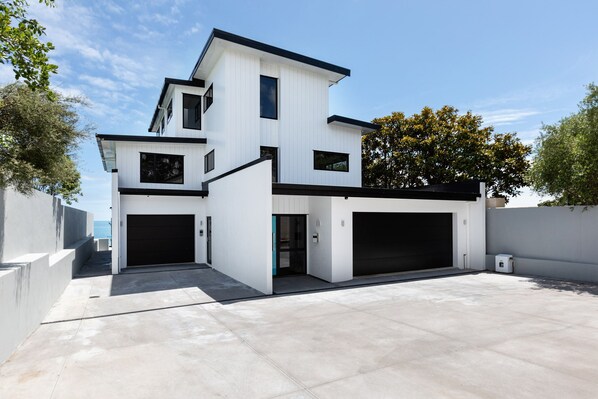 A modern two-story house with a garage, a covered patio, and a view of the sea.