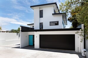 A modern two-story house with a black garage door, a teal door, and a white exterior.