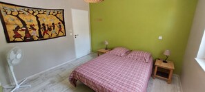 Ein Schlafzimmer mit einem Bett, einem Wandventilator, zwei Nachttischen mit Lampen, einer grünen Wand und einer Tür.