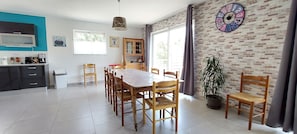 A spacious dining area with a wooden table and chairs, a kitchen with modern appliances, and a brick-patterned wall with a clock. - Villa with pool, 10 persons, fully equipped with calm, clear view (Joyeuse)