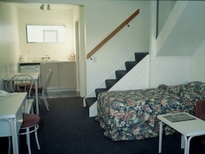 A compact room with a bed, a small table, a chair, and a staircase. - Auckland Akl Airport Motel (Auckland)